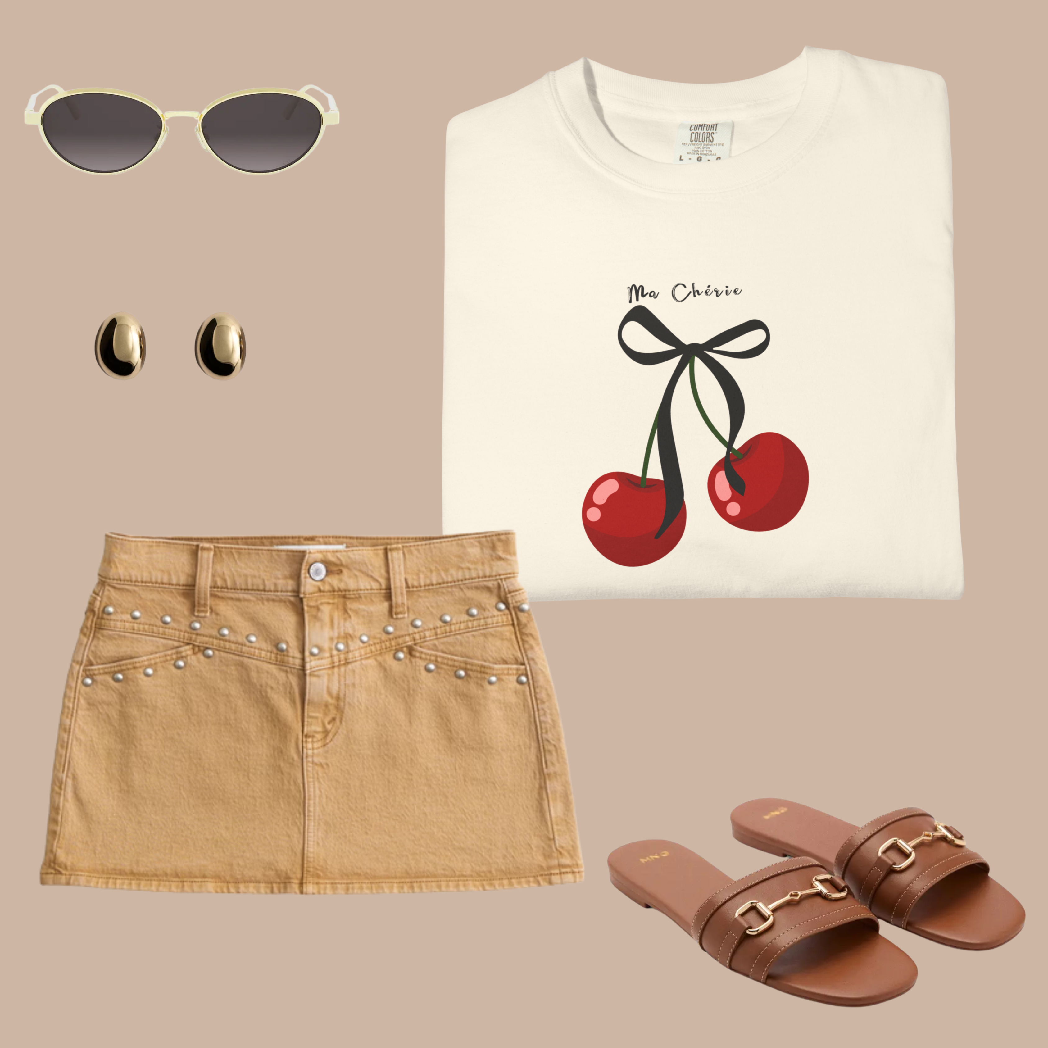 Cream Comfort Colors t-shirt with red cherry and bow design and “Ma Chérie” text, styled with a tan mini skirt, gold earrings, and brown sandals.