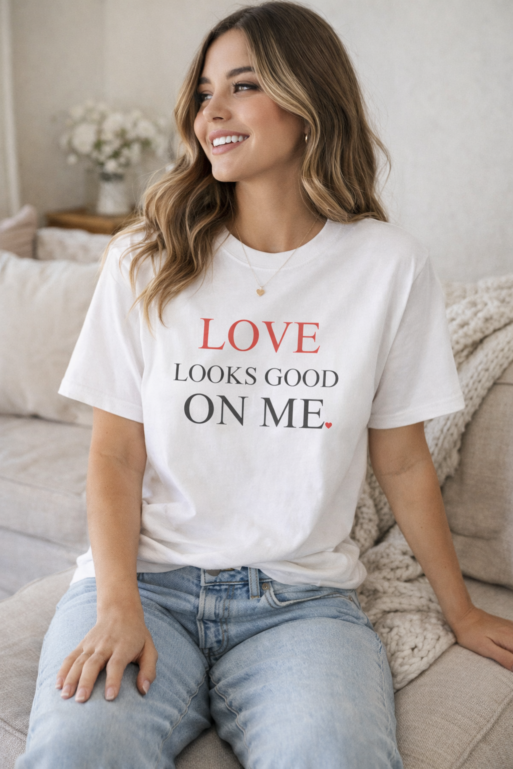 Woman wearing a white t-shirt with 'LOVE LOOKS GOOD ON ME' text, sitting on a couch.