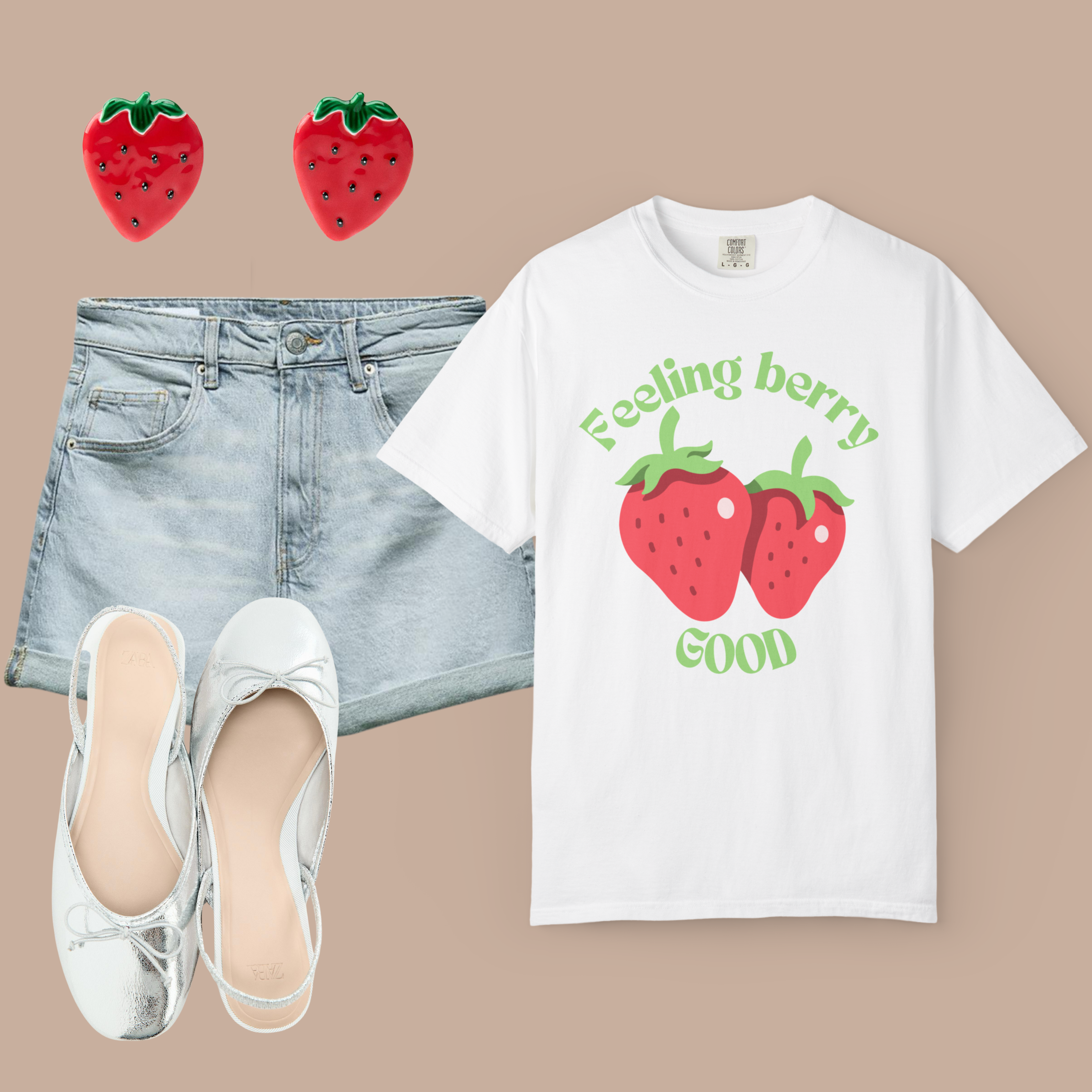 White Comfort Colors t-shirt with strawberry graphic and “Feeling Berry Good” text, styled with denim shorts, silver flats, and strawberry earrings.